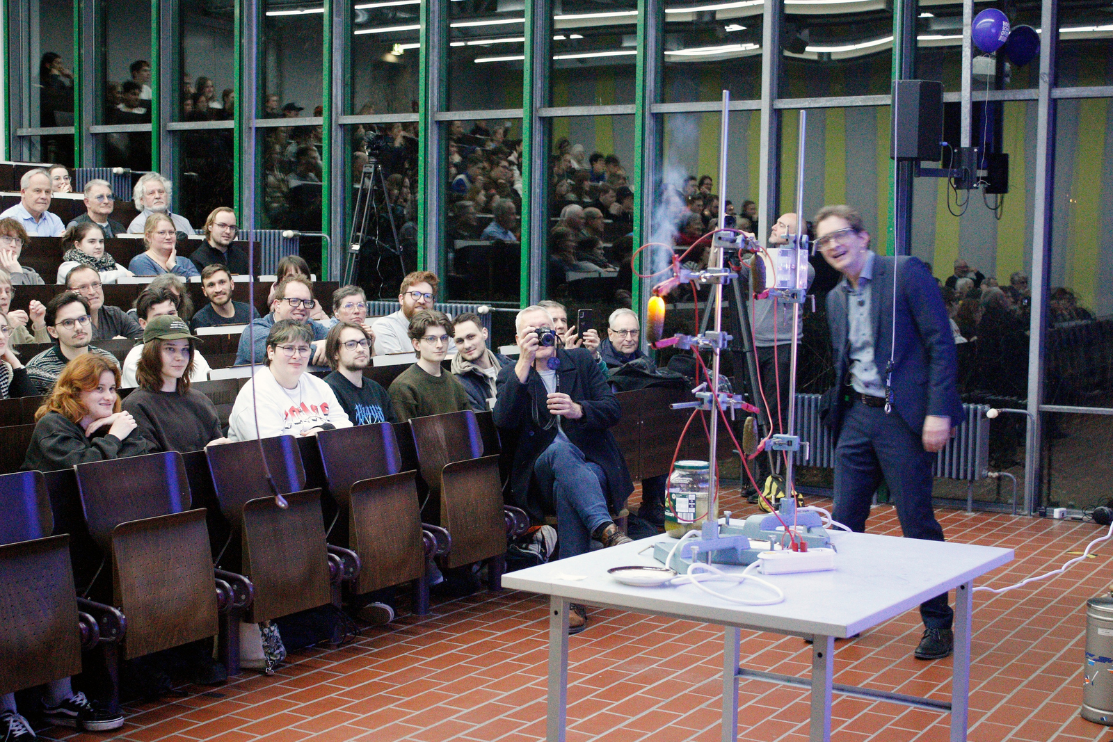In einem Vorlesungssaal sitzende Personen verfolgen ein Experiment mit einer glühenden Gurke