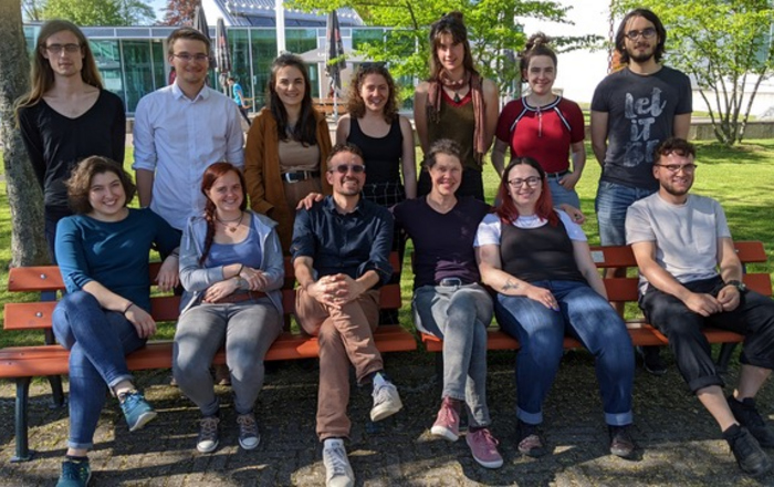 Gruppenfoto der Teilnehmenden, die auf dem Campus Offenburg auf einer Bank sitzen beziehungsweise hinter dieser stehen