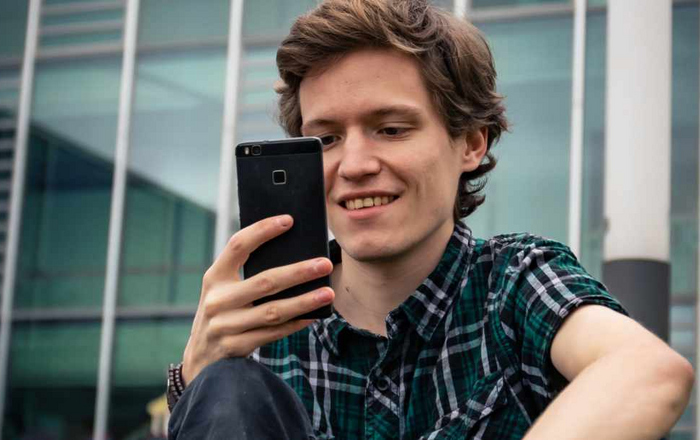 Ein junger Mann schaut vor Gebäude D auf sein Smartphone