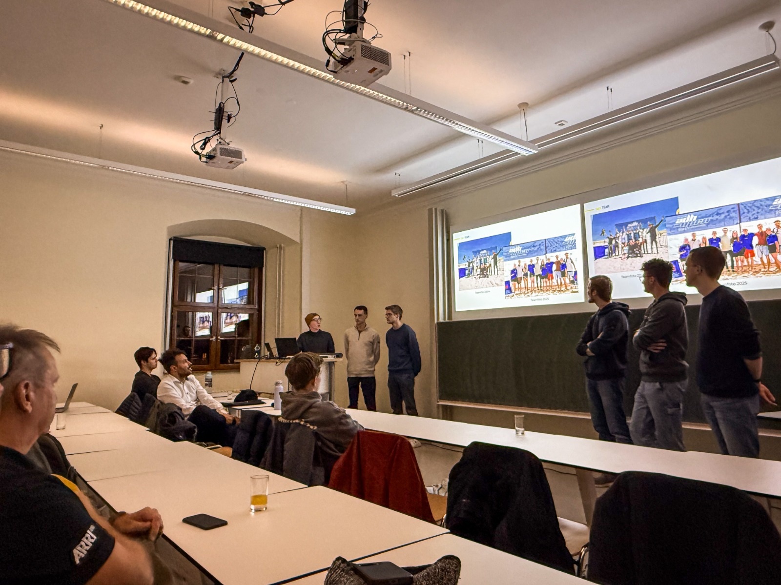 Studierende stehen neben eine Leinwand und erklären sitzenden Zuhörenden eine Präsentation